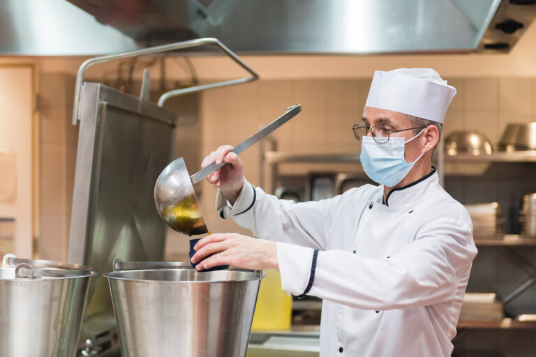 Cuisinier portant un masque chirurgical qui sert de la sauce avec une louche dans une cuisine